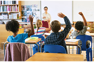 Group of school kids raising hands in classroom